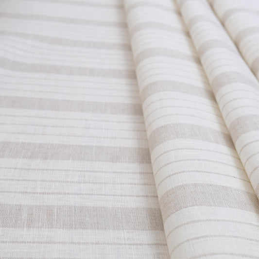Taupe stripe linen fabric folded to showcase its soft airy weave and subtle neutral stripe design. This lightweight material is ideal for sewing curtains, table linens, pillow covers, and cottagecore-inspired home décor. Perfect for DIY sewing projects, rustic farmhouse accents, neutral minimalist interiors, and versatile décor crafts where natural linen texture adds charm and durability.