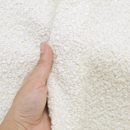 A hand is holding a close-up view of a white, fluffy fabric, possibly a blanket or a towel.