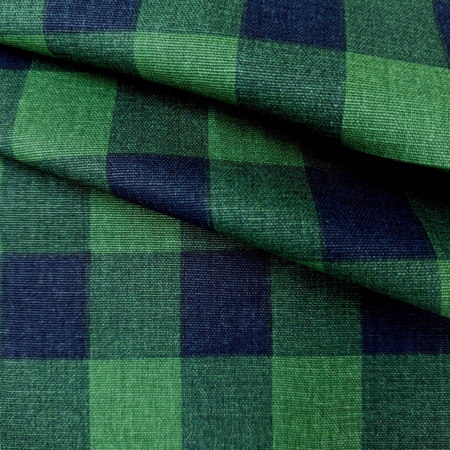 a close-up view of a fabric with a green and blue checkered pattern. The fabric appears to be folded or crumpled, creating a textured and visually interesting surface.