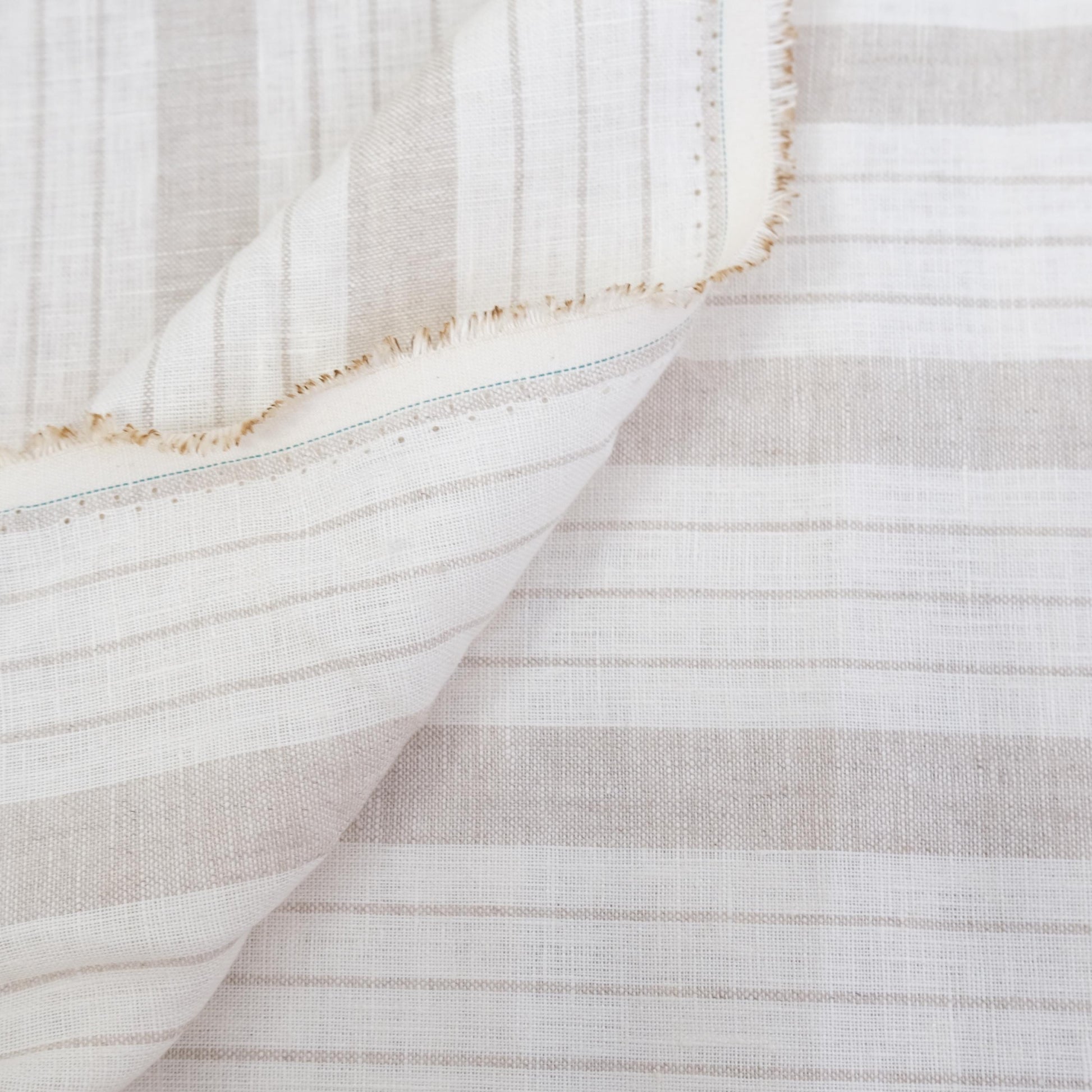 Taupe stripe linen fabric styled in folds, showing airy drape, breathable weave, and soft neutral tones. This striped fabric is ideal for farmhouse table décor, minimalist curtains, cottage-inspired napkins, and rustic DIY home projects. The natural linen texture and classic stripe design make it a versatile material for sewing projects that require elegance and durability, such as lightweight drapery, tablecloths, or soft furnishings.