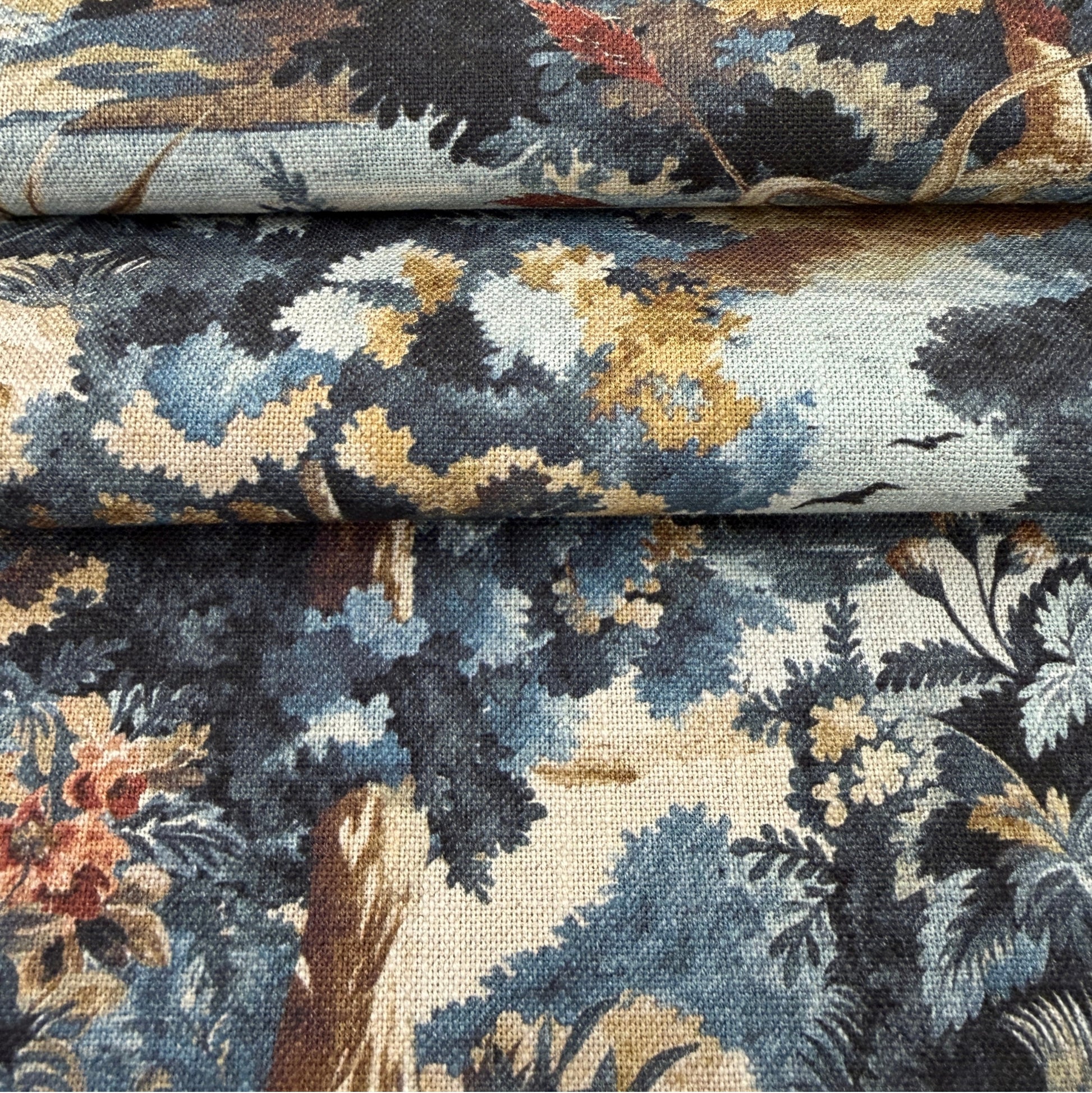 The image is a close-up of a fabric with a floral pattern, featuring a mix of blue, green, and brown colors.