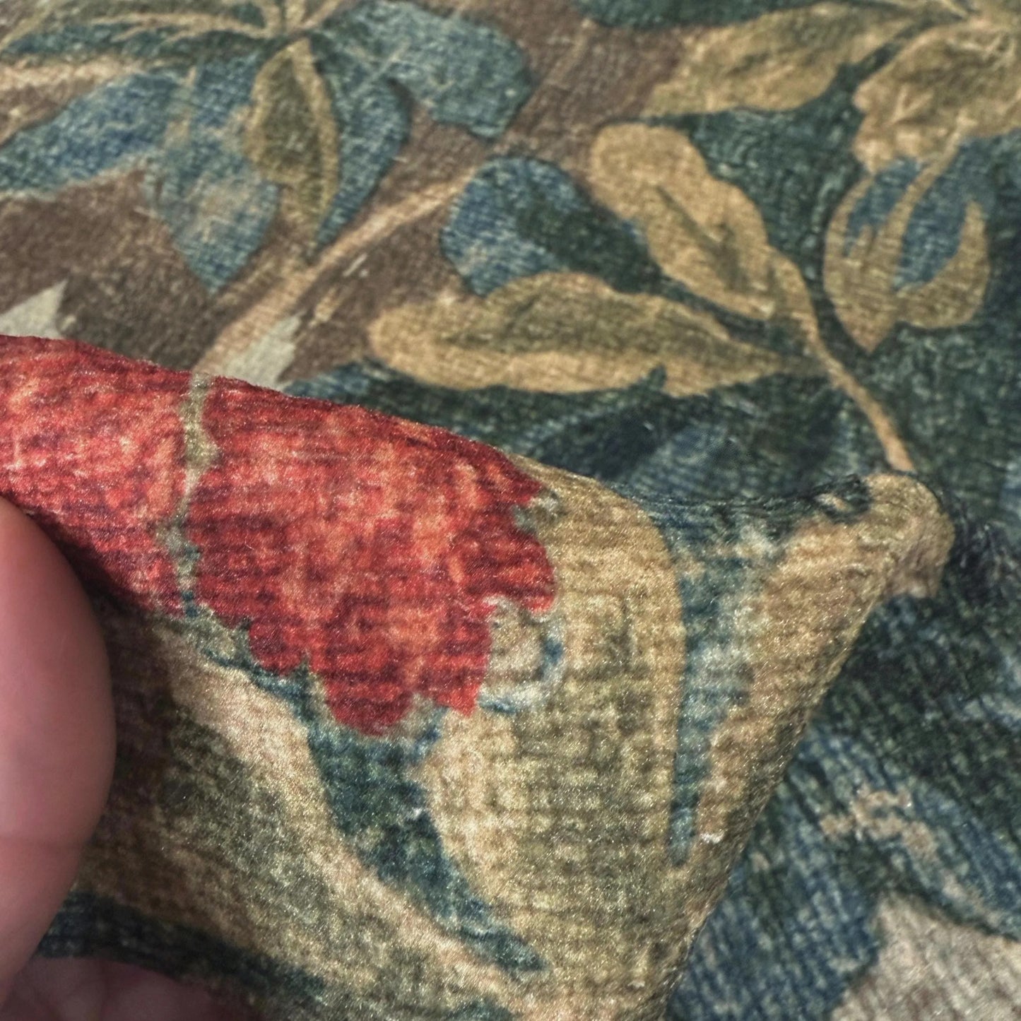A close-up view of a fabric with a floral pattern, featuring a red flower and green leaves.