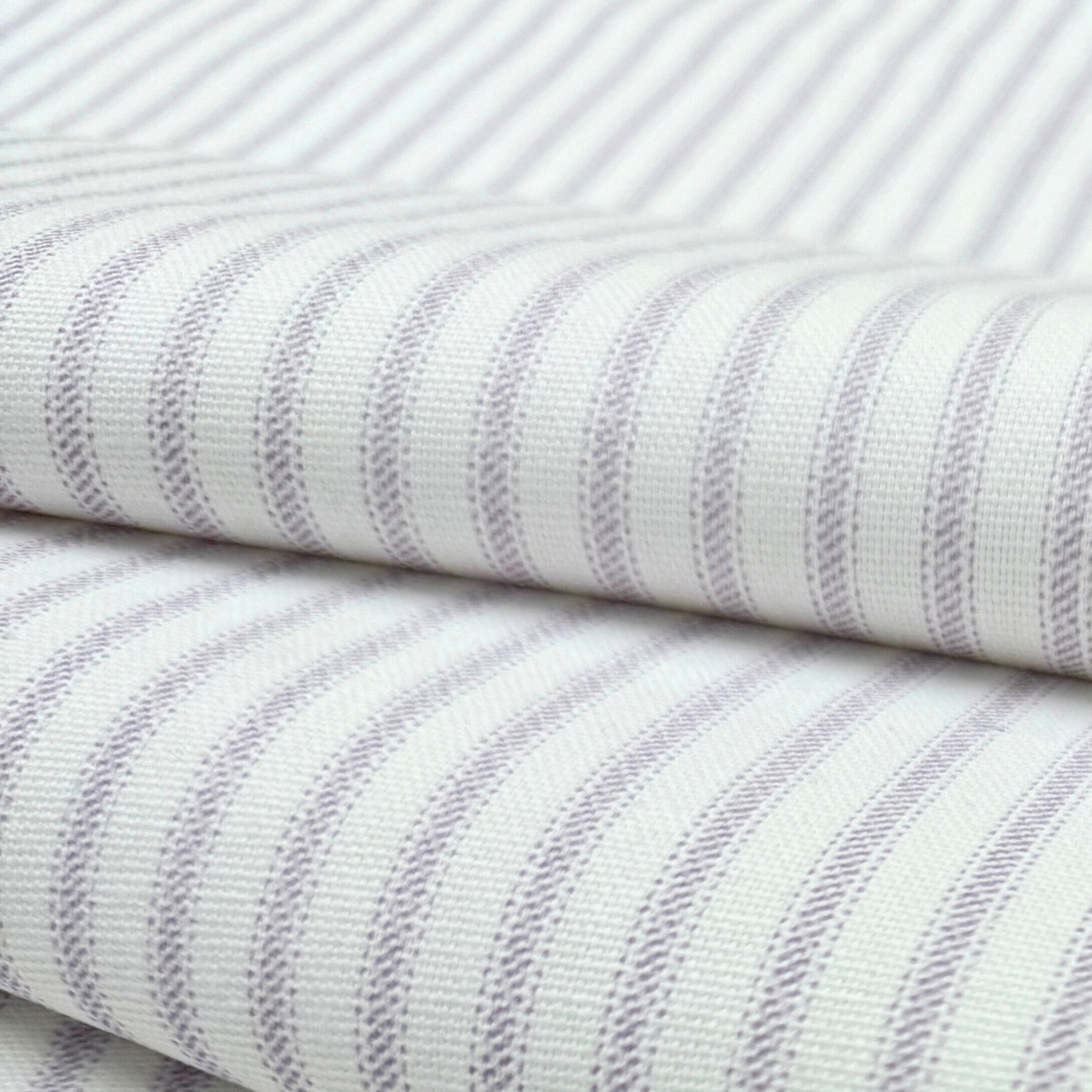 a close-up view of a fabric with a striped pattern in shades of white and purple. The fabric appears to be folded or rolled, with the edges of the fabric visible.