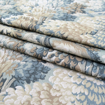 a close-up view of a fabric with a floral pattern in shades of blue, green, and beige. The fabric appears to be folded or rolled, revealing the intricate design and texture of the material.