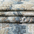 a close-up view of a fabric with a floral pattern in shades of blue, green, and beige. The fabric appears to be folded or rolled, revealing the intricate design and texture of the material.