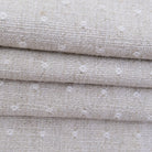 A close-up view of a fabric with a textured, woven pattern in shades of beige and white.