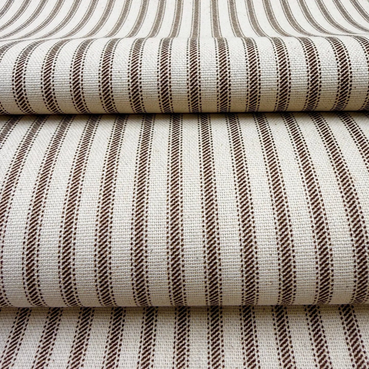 a close-up view of a fabric with a striped pattern in shades of brown and white. The fabric appears to be folded or stacked, creating a layered effect.