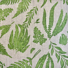 a close-up view of a fabric with a repeating pattern of green fern leaves and other green plant-like leaves. The pattern is intricate and detailed, creating a visually appealing and natural-looking design.