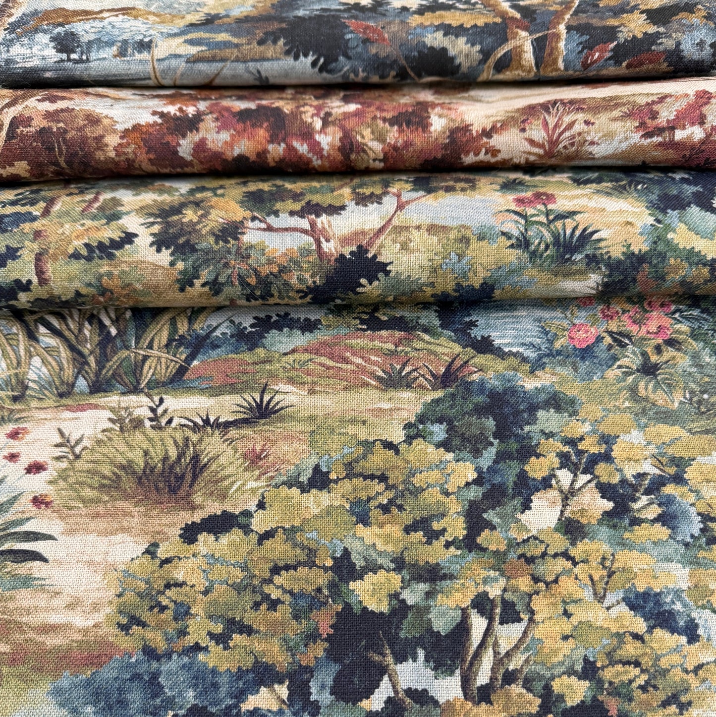 a close-up view of a fabric with a detailed landscape pattern, including trees, bushes, and flowers in various shades of green, brown, and red.