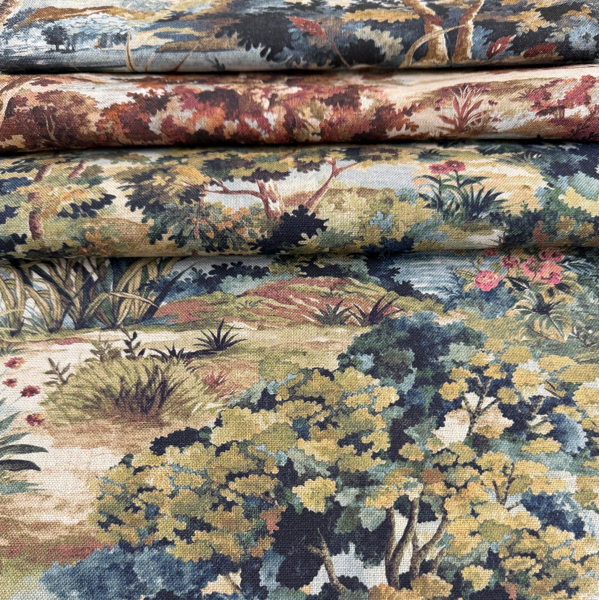 a close-up view of a fabric with a detailed landscape pattern, including trees, bushes, and flowers in various shades of green, brown, and red.