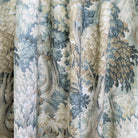a close-up view of a fabric with a floral pattern in shades of blue, green, and beige. The fabric appears to be made of a woven material, with a textured and intricate design.