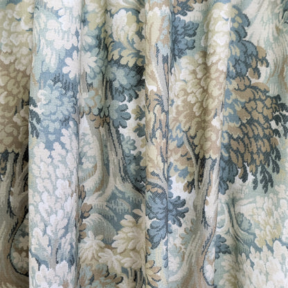 a close-up view of a fabric with a floral pattern in shades of blue, green, and beige. The fabric appears to be made of a woven material, with a textured and intricate design.