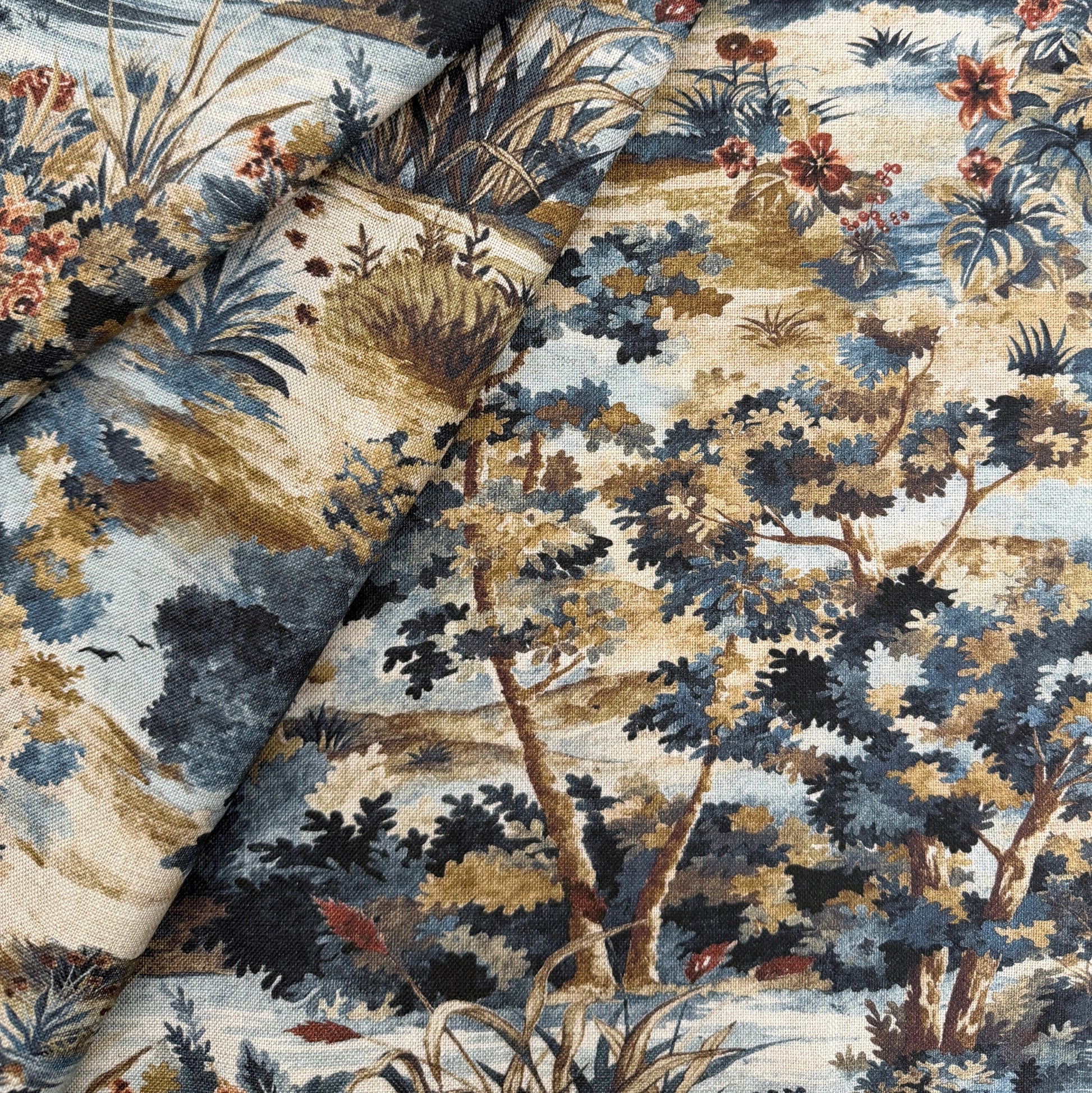 The image is a close-up of a fabric with a detailed, colorful pattern of trees, flowers, and foliage. The fabric appears to be a piece of clothing or textile, with the pattern and colors suggesting a natural, outdoor setting.
