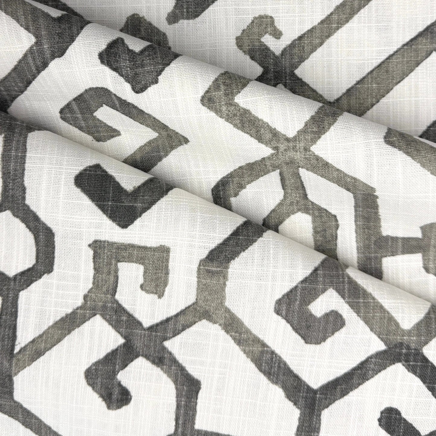 a close-up view of a fabric with a repeating geometric pattern in shades of gray and white. The pattern consists of various shapes and lines, creating a visually striking and intricate design.