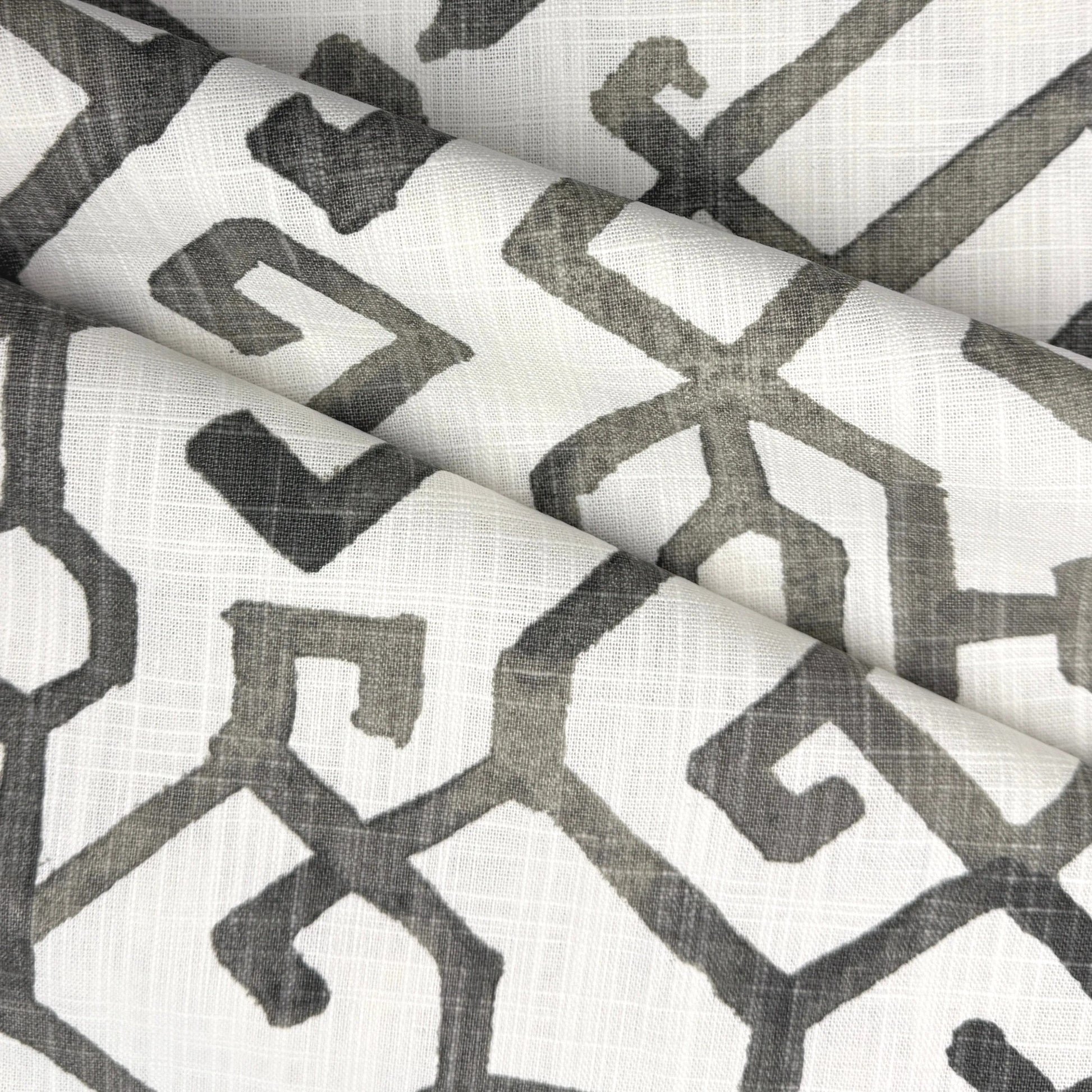 a close-up view of a fabric with a repeating geometric pattern in shades of gray and white. The pattern consists of various shapes and lines, creating a visually striking and intricate design.