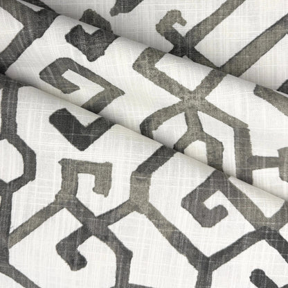 a close-up view of a fabric with a repeating geometric pattern in shades of gray and white. The pattern consists of various shapes and lines, creating a visually striking and intricate design.