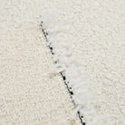 A close-up view of a white, fluffy fabric with a black fringed edge, creating a textured and visually interesting surface.