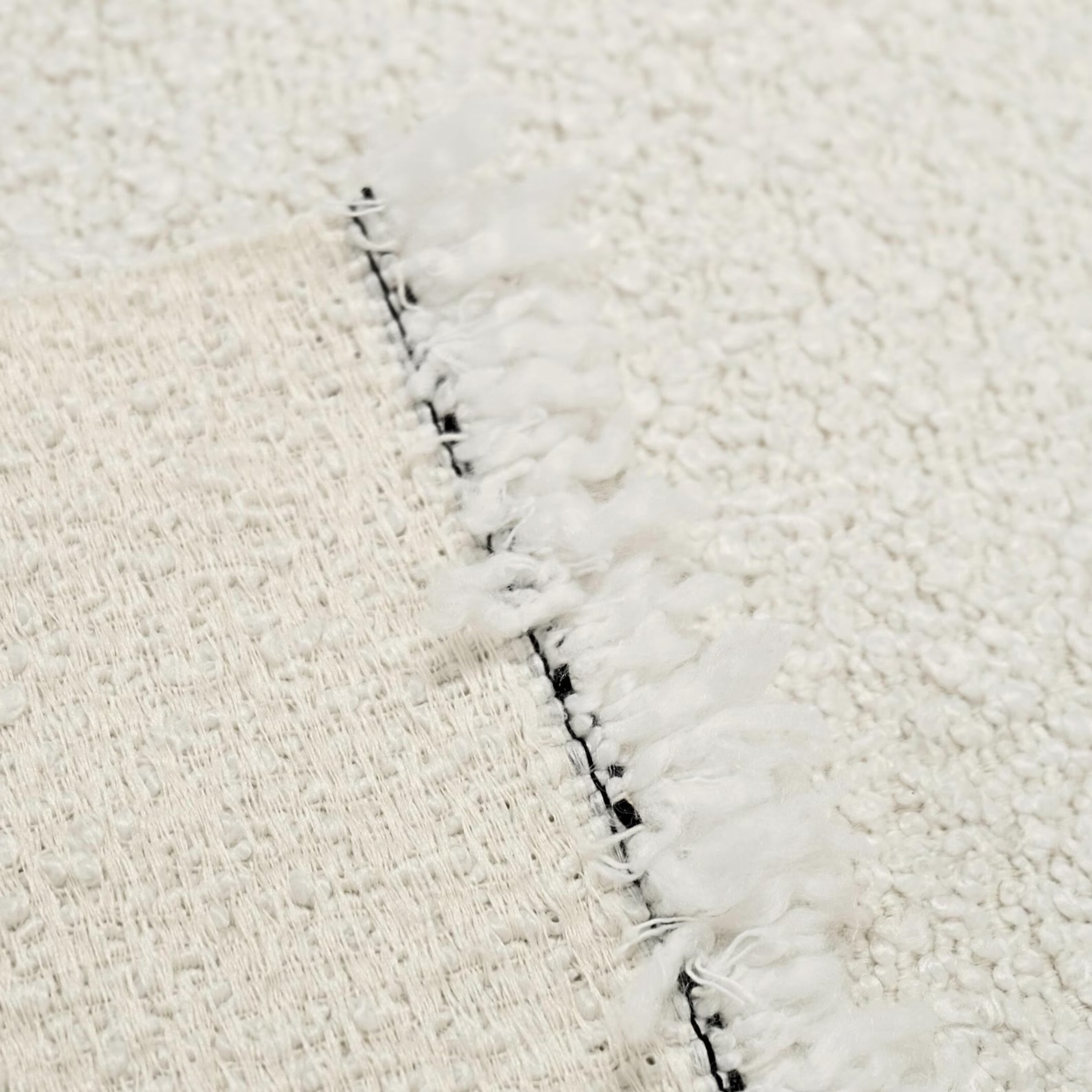 A close-up view of a white, fluffy fabric with a black fringed edge, creating a textured and visually interesting surface.