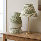 a wooden table with a lamp and a stack of green and white patterned lampshades on it.