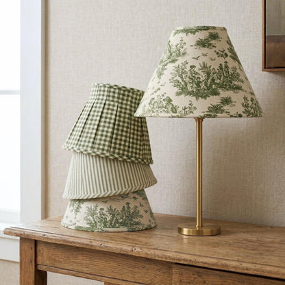 a wooden table with a lamp and a stack of green and white patterned lampshades on it.