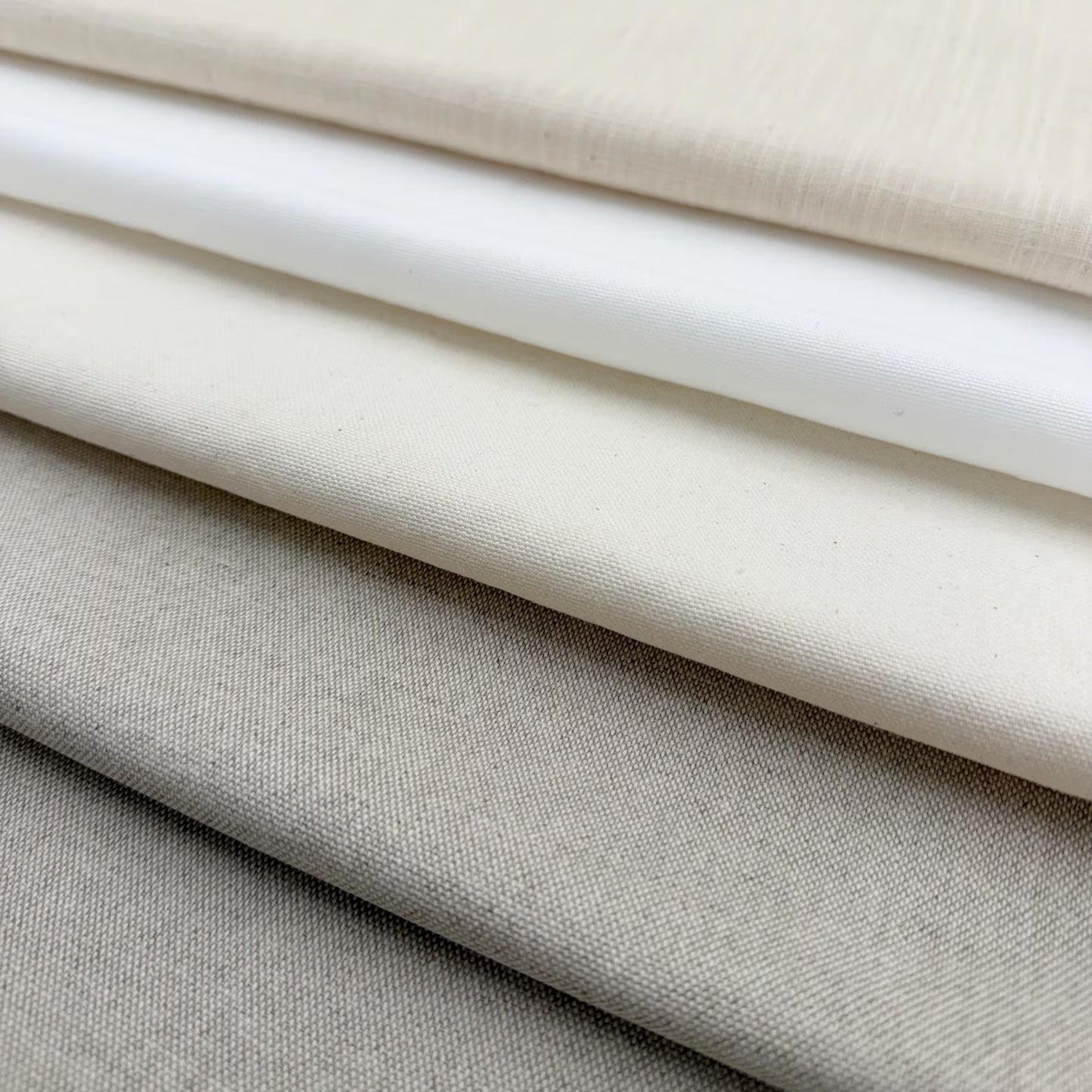 A close-up image of various fabric swatches in shades of white, gray, and beige, arranged in a layered fashion.