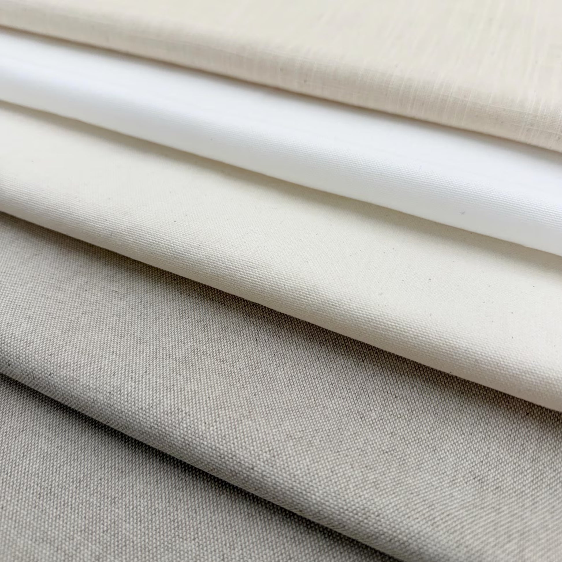 A close-up image of various fabric swatches in shades of white, gray, and beige, arranged in a layered fashion.