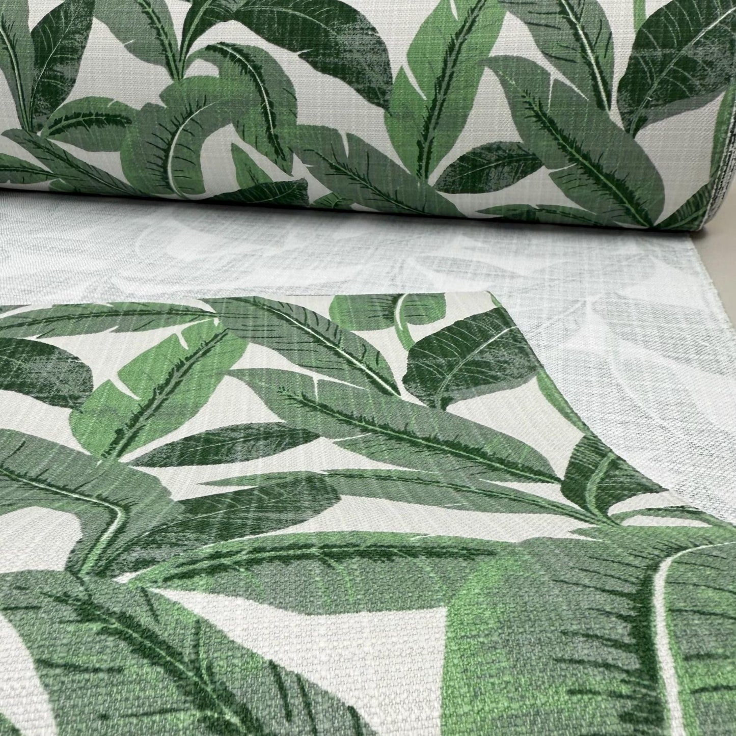 a close-up view of a fabric with a repeating pattern of green leaves, likely palm leaves, against a white background.