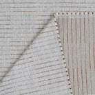 a close-up view of a fabric with a striped pattern, featuring a diagonal line running across it. The fabric appears to be made of a light-colored material, possibly linen or cotton, with a textured appearance.