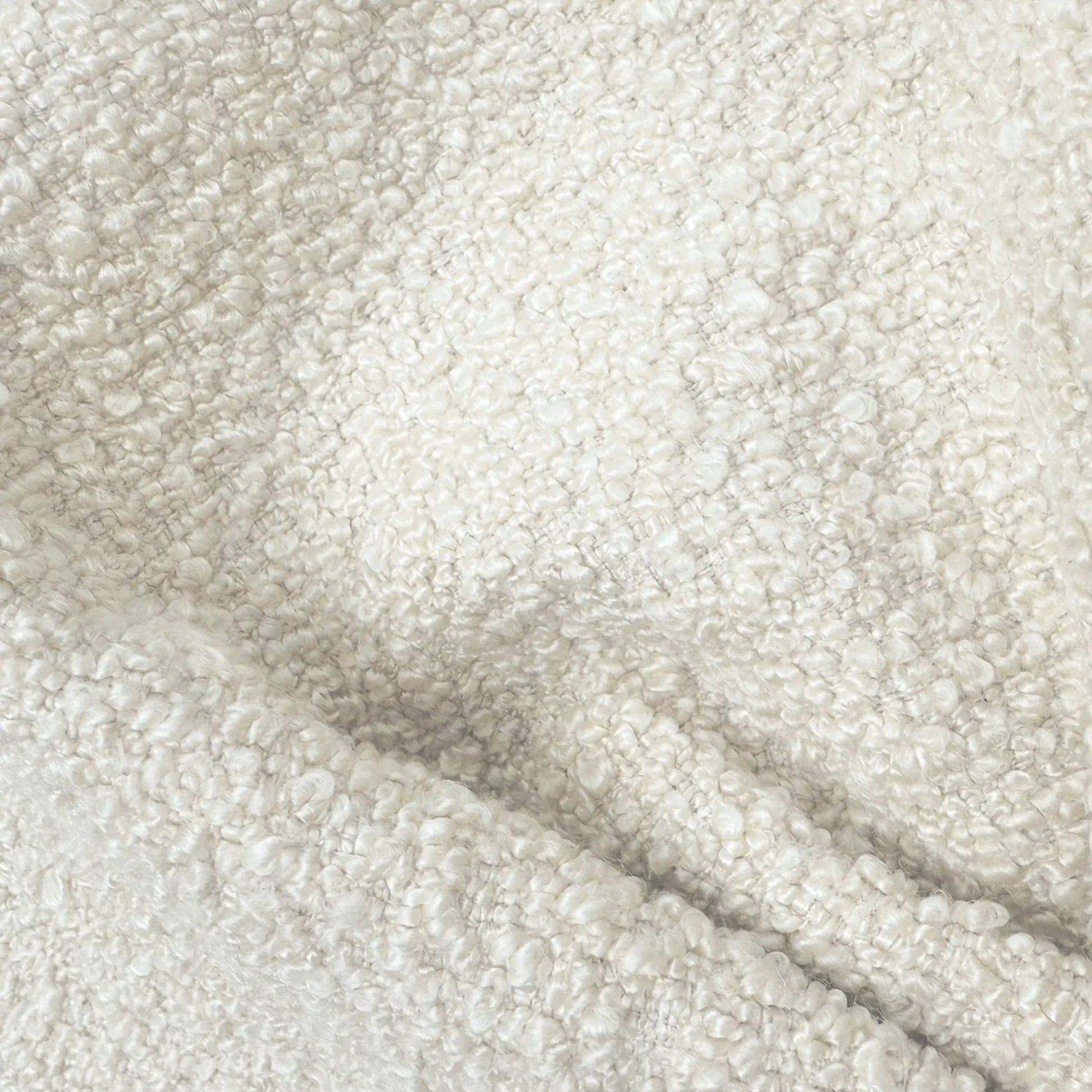a close-up view of a soft, fluffy, and textured fabric, possibly a white or cream-colored material. The fabric appears to be made of a fuzzy or woolly texture, giving it a cozy and comfortable appearance.