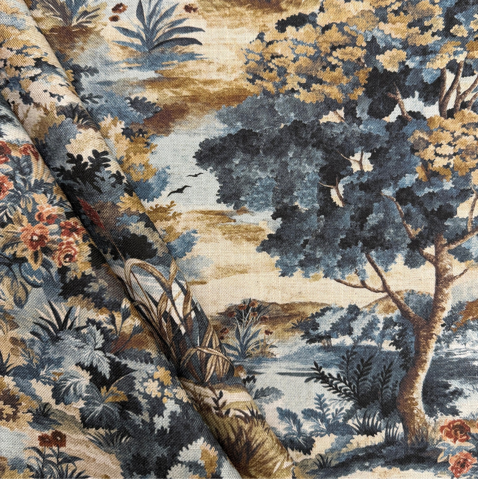 The image is a close-up of a fabric with a detailed landscape scene printed on it. The fabric features a variety of colors, including shades of blue, green, and brown, as well as intricate patterns and textures. The scene depicts a lush, natural landscape with trees, flowers, and a body of water, creating a sense of depth and complexity. The fabric appears to be a piece of textile art, showcasing the skill and craftsmanship involved in its creation.