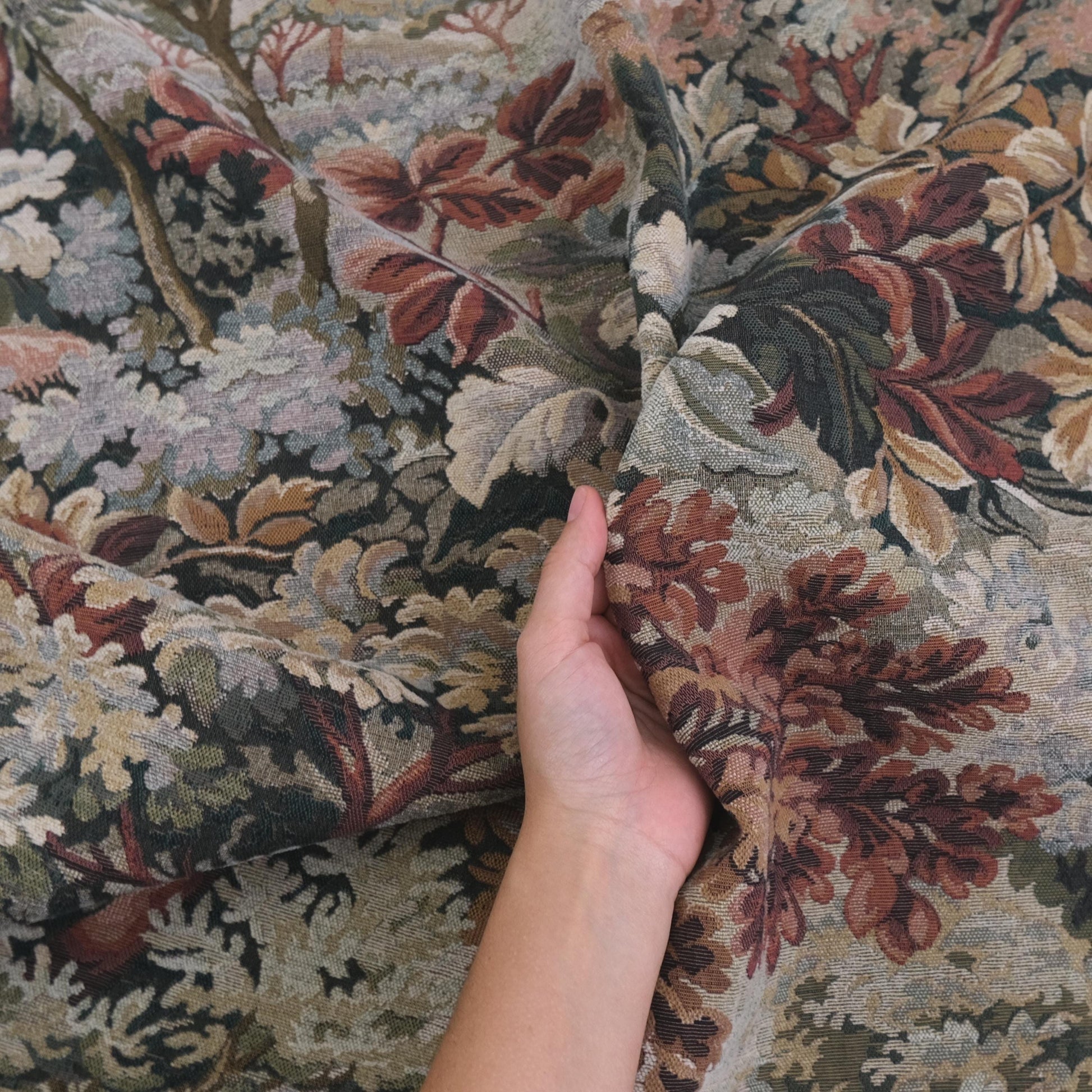 Hand holding heavyweight tapestry upholstery fabric in Woodrose foliage pattern, woven jacquard textile with scenic verdure design, antique style upholstery material perfect for sofas, armchairs, ottomans, curtains, wall hangings, and furniture restoration projects.