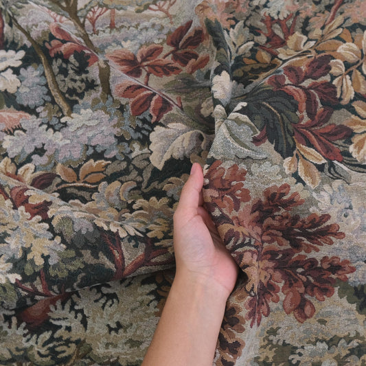 Hand holding heavyweight tapestry upholstery fabric in Woodrose foliage pattern, woven jacquard textile with scenic verdure design, antique style upholstery material perfect for sofas, armchairs, ottomans, curtains, wall hangings, and furniture restoration projects.