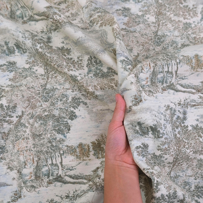 A hand is holding a fabric with a pattern of trees and foliage, suggesting it is a piece of clothing or textile with a nature-inspired design.