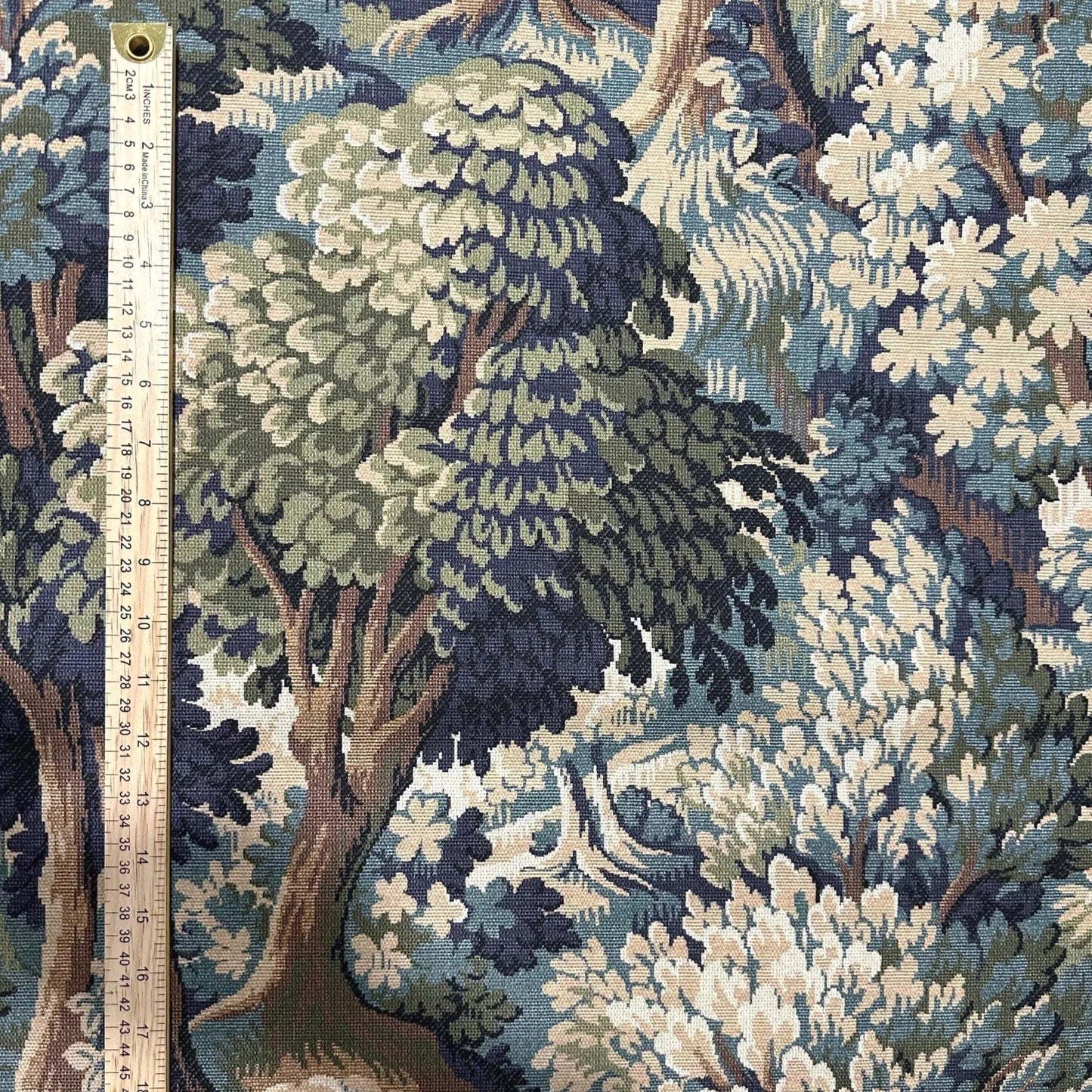 a detailed tapestry or fabric with a lush, forest-like scene, including trees, bushes, and flowers in various shades of green, blue, and brown. The fabric appears to be a textile or fabric with a natural, botanical motif.