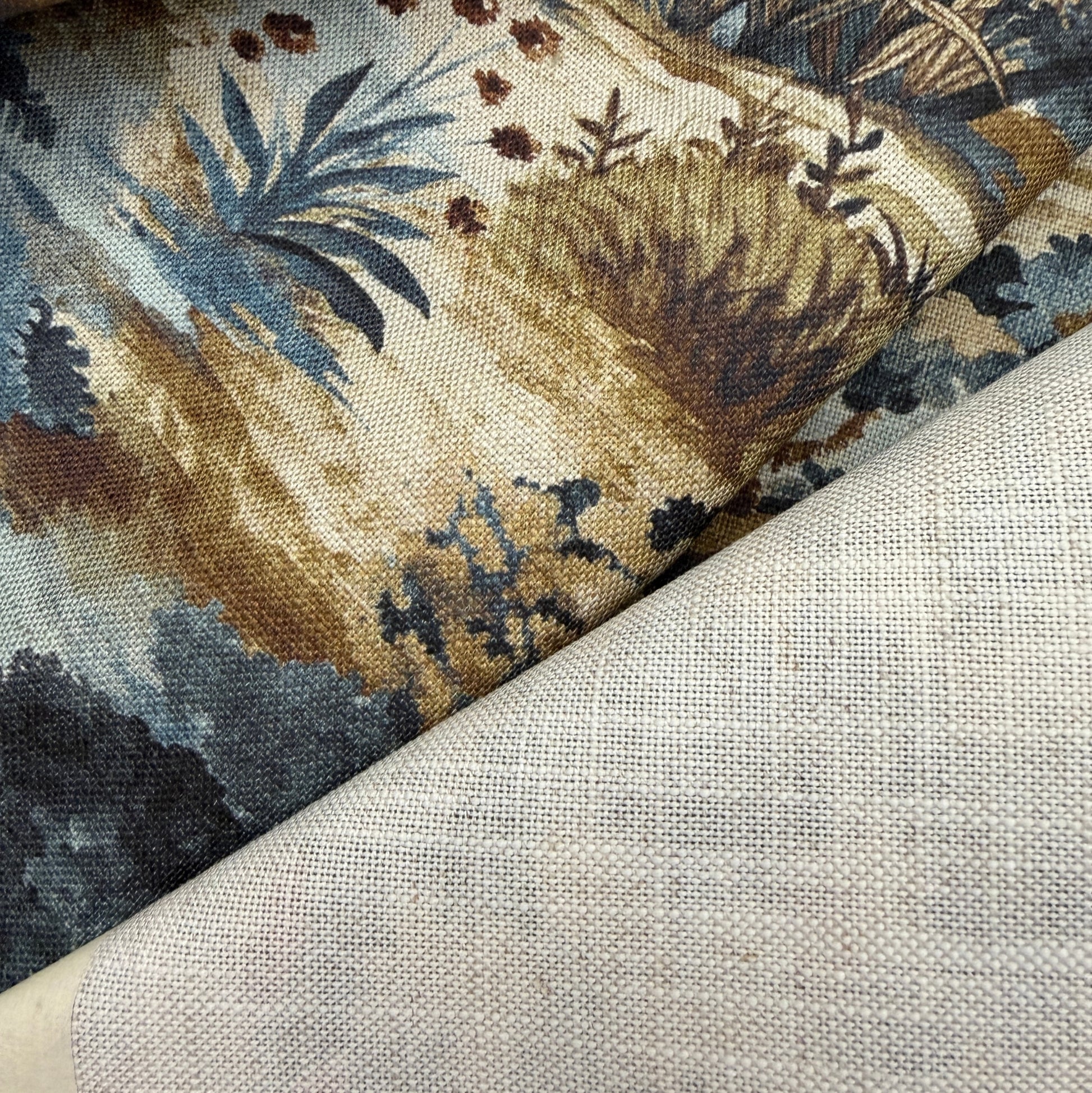 a close-up view of a fabric with a floral pattern, featuring various shades of blue, brown, and green. The fabric appears to be a piece of linen or a similar material, with a textured and woven appearance.