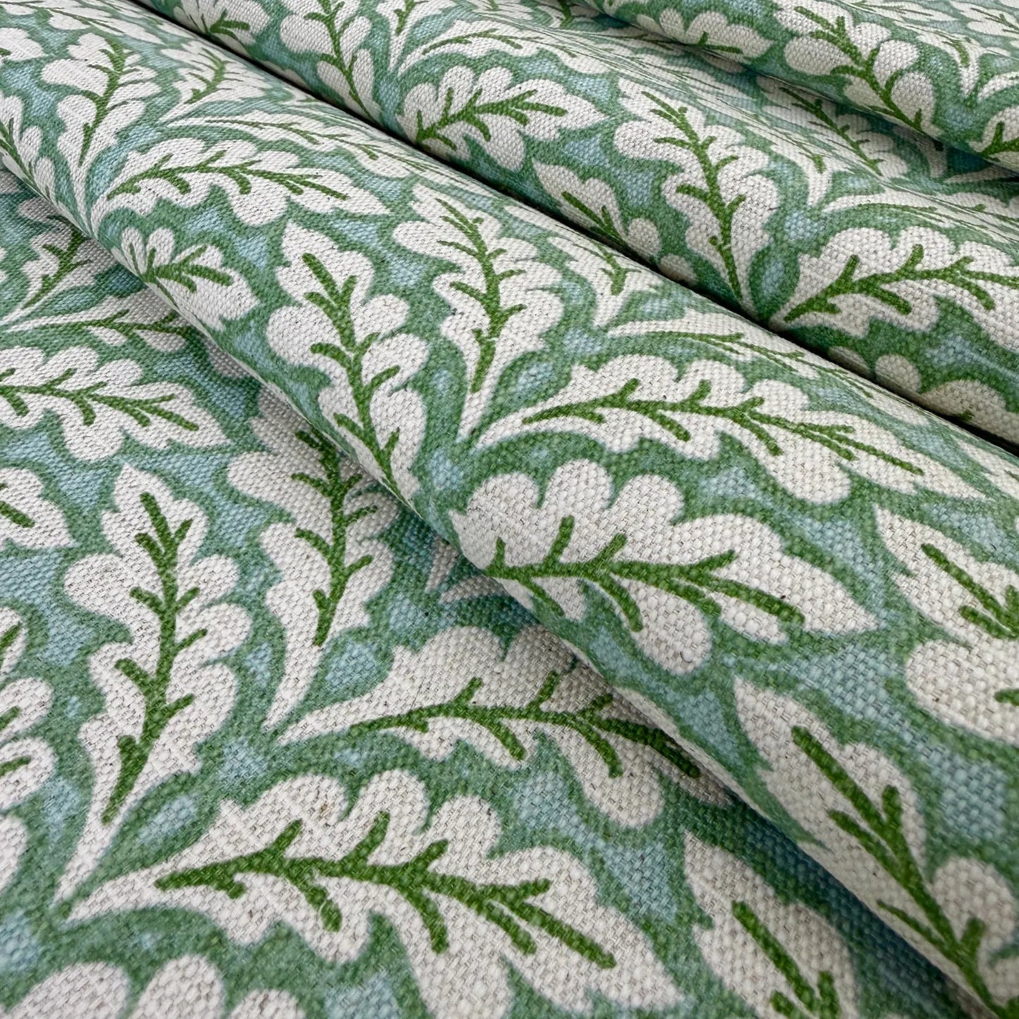 a close-up view of a fabric with a repeating pattern of green leaves and white flowers. The pattern is intricate and detailed, with the leaves and flowers arranged in a way that creates a visually appealing design. The fabric appears to be made of a soft, textured material, suitable for use in clothing or home decor.