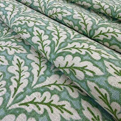 a close-up view of a fabric with a repeating pattern of green leaves and white flowers. The pattern is intricate and detailed, with the leaves and flowers arranged in a way that creates a visually appealing design. The fabric appears to be made of a soft, textured material, suitable for use in clothing or home decor.