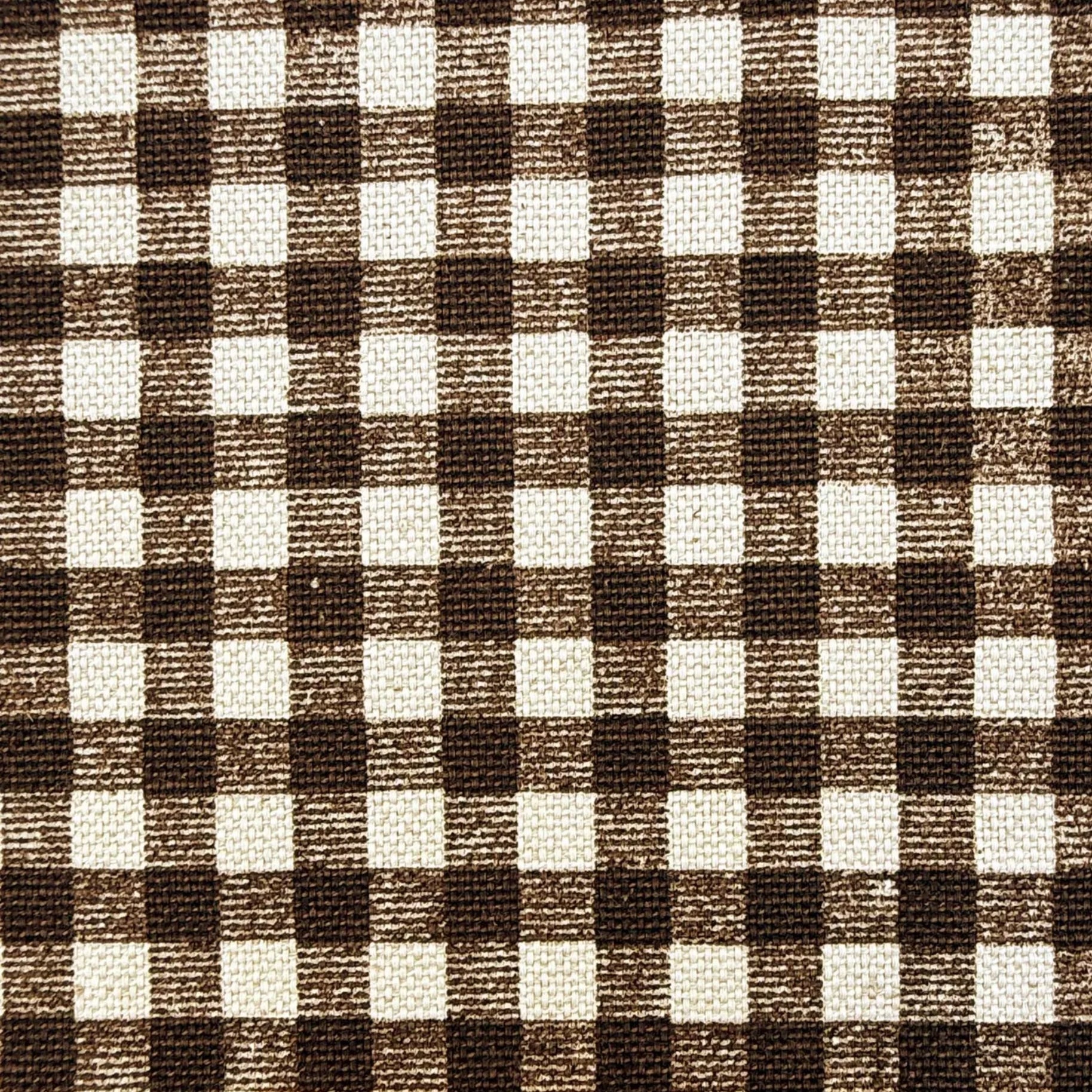 a close-up view of a fabric with a checkered pattern in shades of brown and white. A ruler is placed next to the fabric to provide a scale for size comparison.