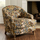 A floral patterned armchair with a wooden frame and legs, placed in front of a fireplace.
