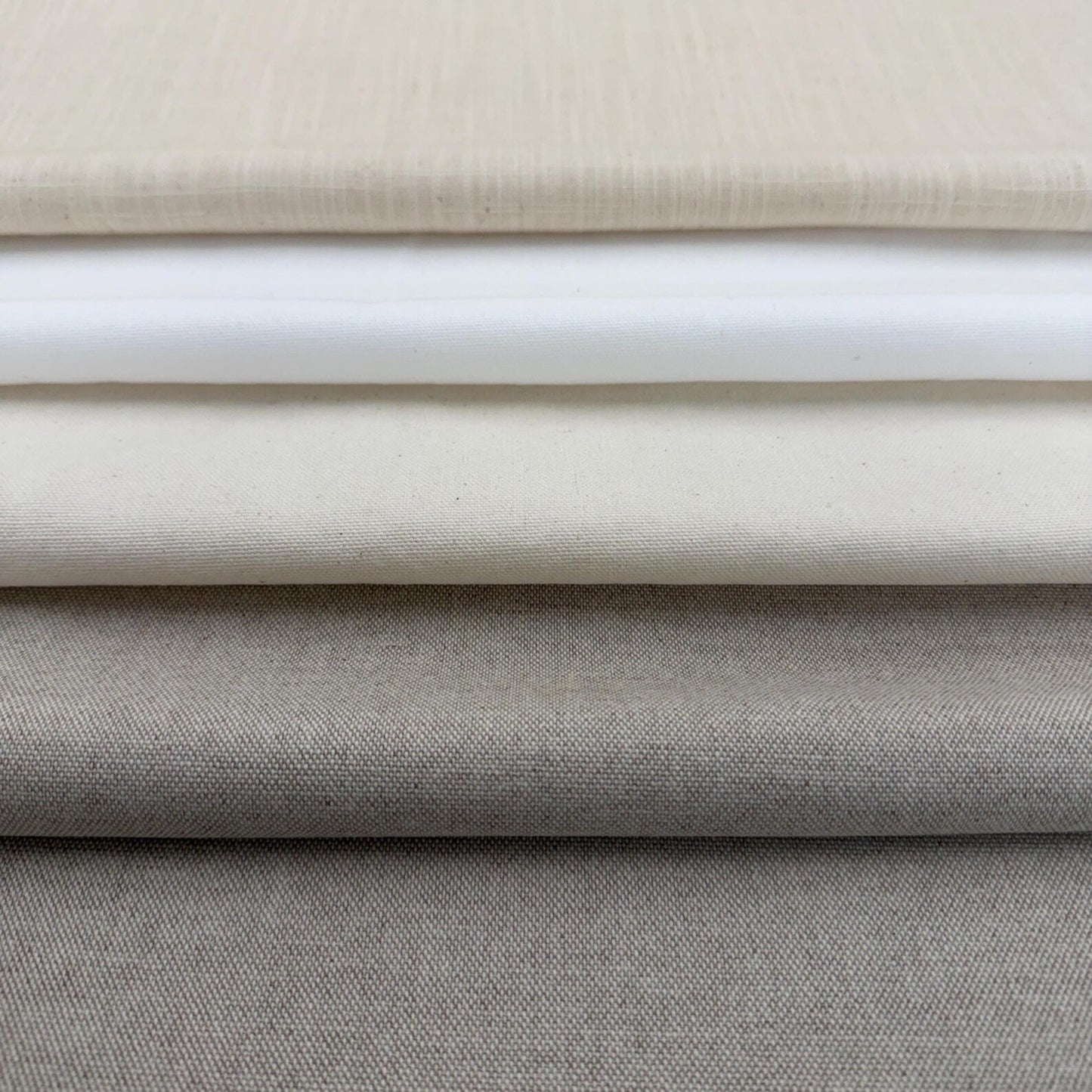 A close-up image of a stack of fabric swatches in various shades of gray and beige.