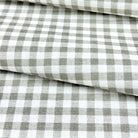 a close-up view of a fabric with a checkered pattern in shades of gray and white. The fabric appears to be folded or rolled, creating a layered effect.