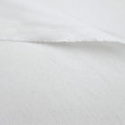 A close-up view of a white fabric, possibly cotton, with a slightly wrinkled texture.