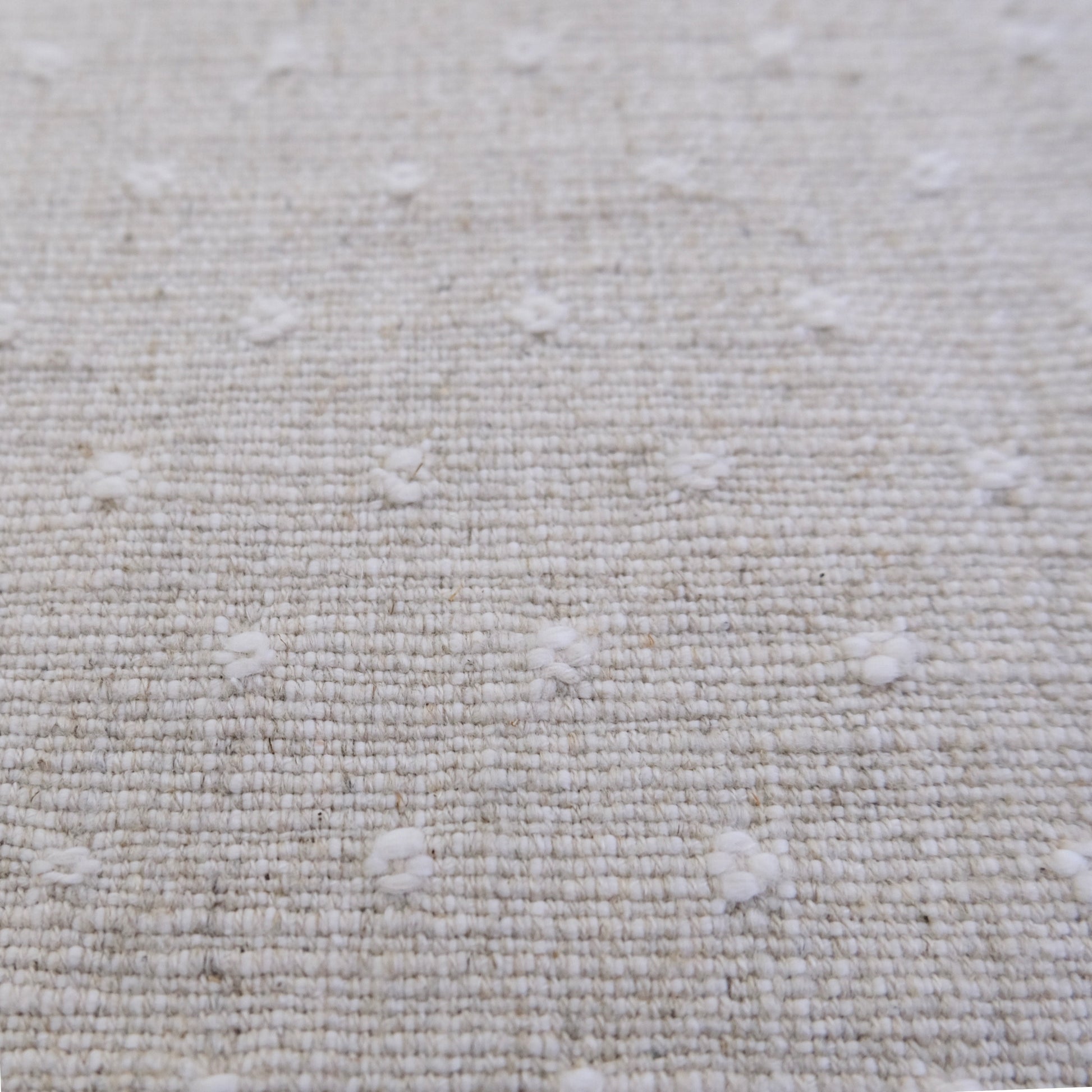 a close-up view of a beige fabric with small white dots or circles scattered across it, creating a textured and patterned appearance.