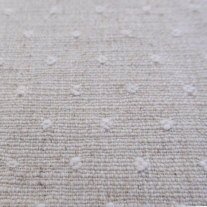 a close-up view of a beige fabric with small white dots or circles scattered across it, creating a textured and patterned appearance.