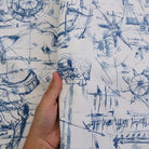A hand is holding a piece of fabric with a blue and white abstract pattern featuring various shapes, lines, and symbols.
