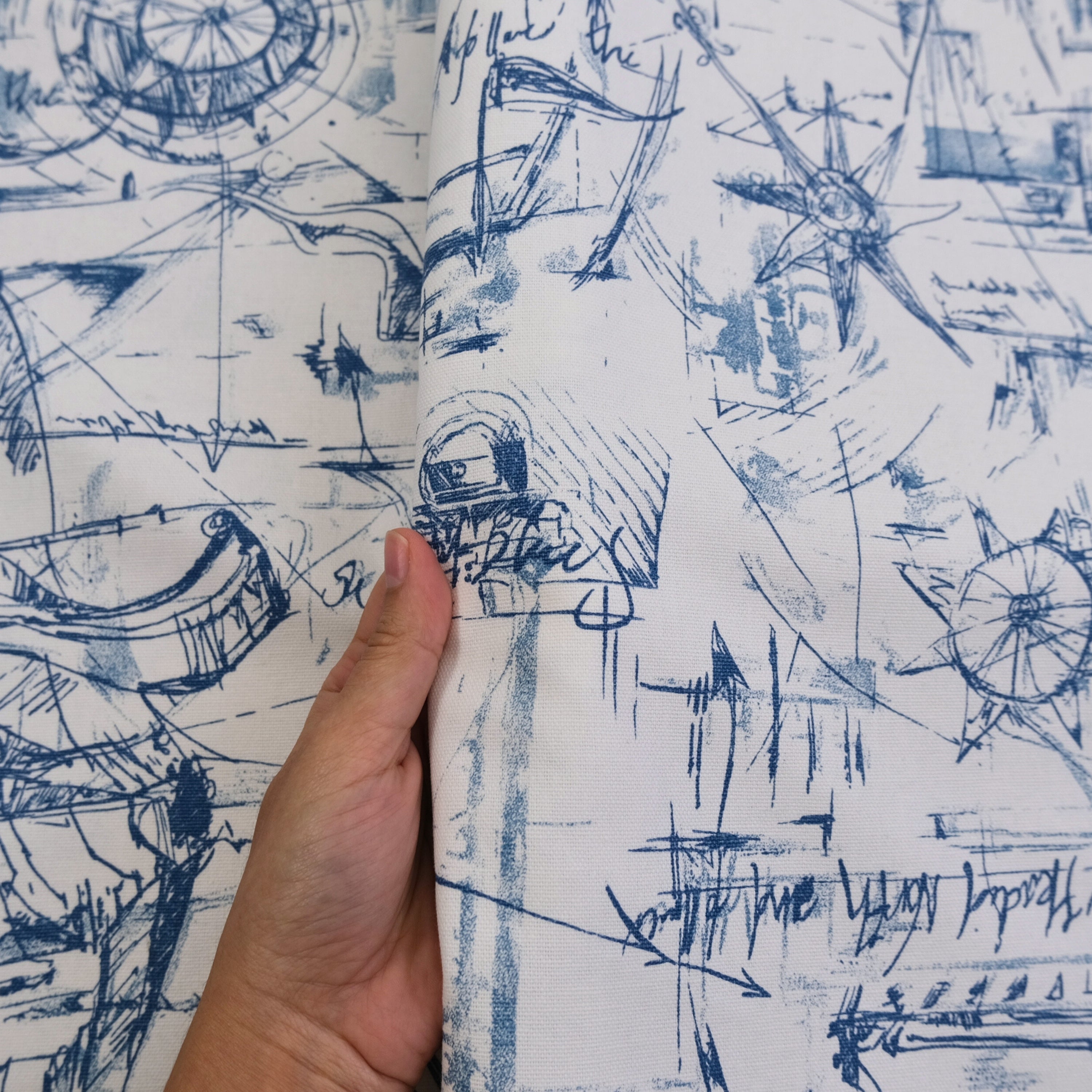 A hand is holding a piece of fabric with a blue and white abstract pattern featuring various shapes, lines, and symbols.