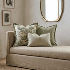 a beige sofa with a decorative pillow and a striped pillow, set against a wall with a large mirror above it.