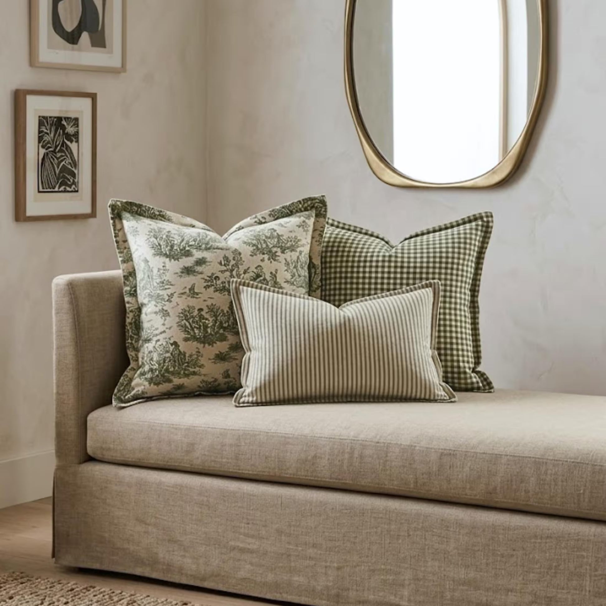 a beige sofa with a decorative pillow and a striped pillow, set against a wall with a large mirror above it.