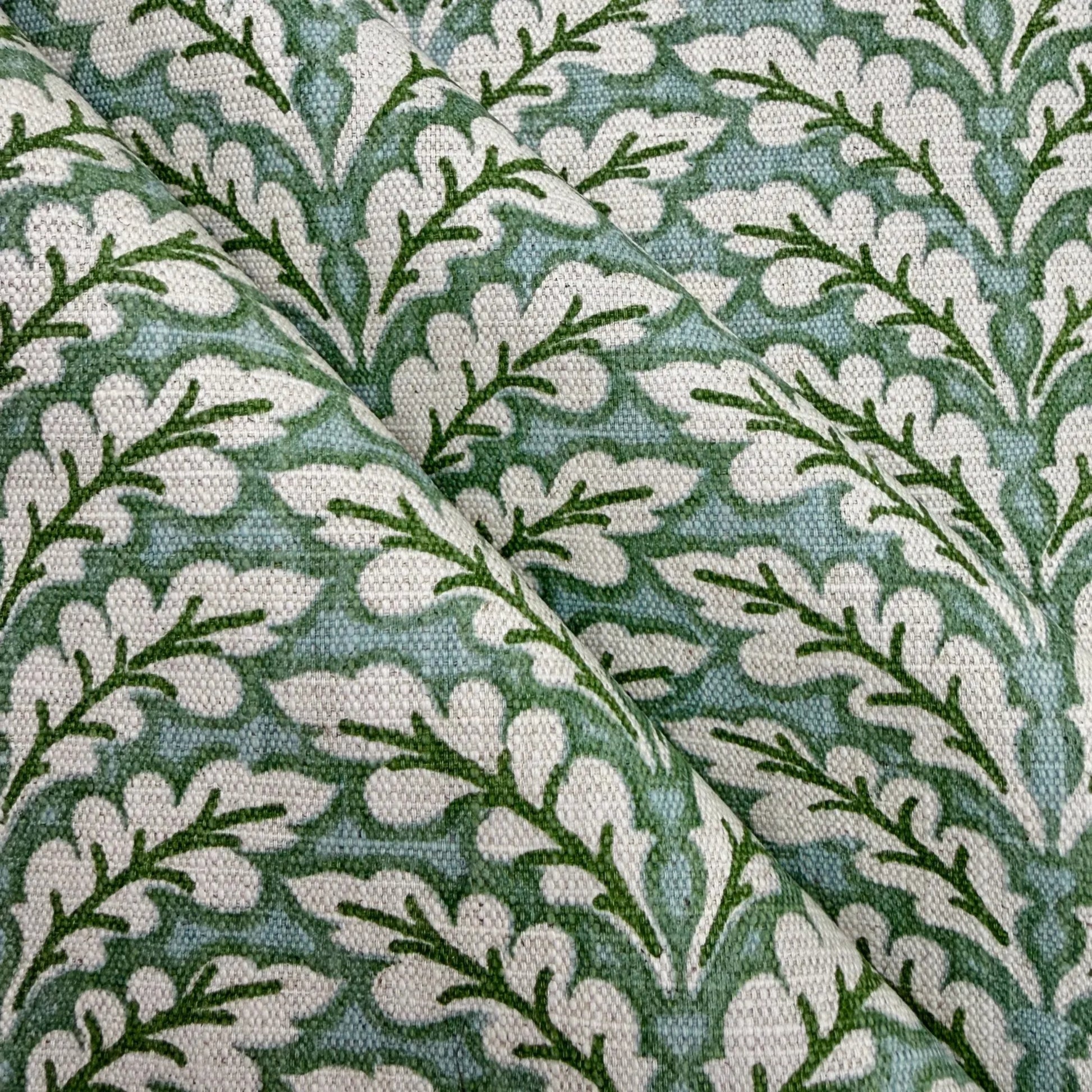 a close-up view of a fabric with a repeating pattern of green leaves and white flowers. The pattern is intricate and detailed, with the leaves and flowers arranged in a repeating design across the fabric's surface.