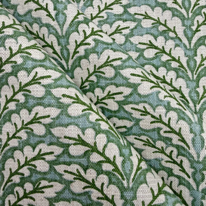 a close-up view of a fabric with a repeating pattern of green leaves and white flowers. The pattern is intricate and detailed, with the leaves and flowers arranged in a repeating design across the fabric's surface.